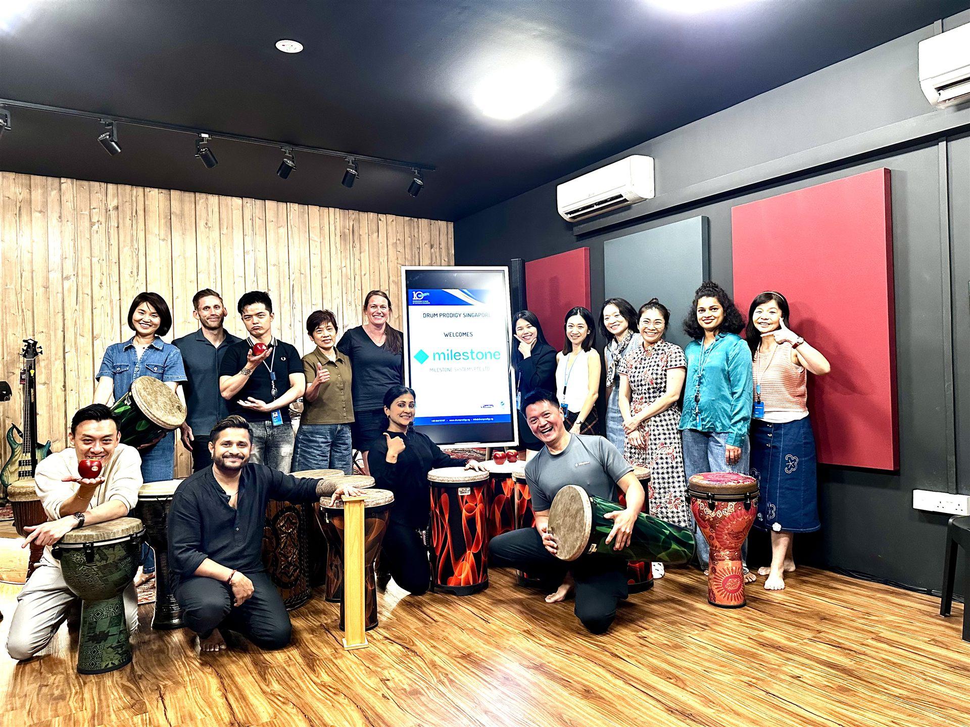 A corporate team drumming together in a Beat and Breathe session, with the client's branding on screen